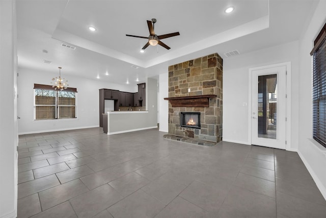 unfurnished living room featuring dark tile patterned floors, ceiling fan with notable chandelier, a fireplace, and a tray ceiling