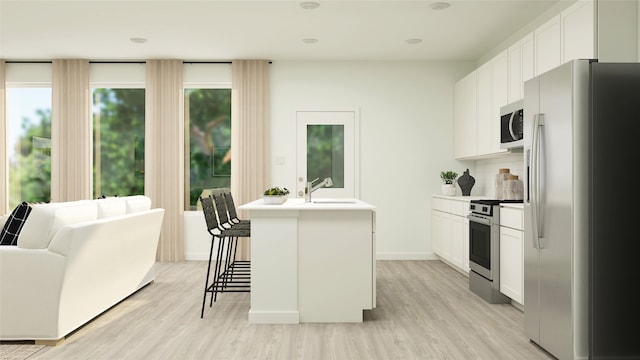 kitchen with a breakfast bar area, appliances with stainless steel finishes, a kitchen island with sink, light hardwood / wood-style floors, and white cabinets