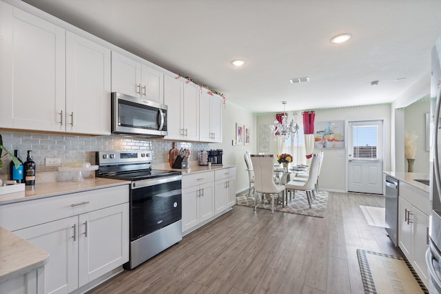 305 Grenada Lake Dr, Princeton, TX 75407 - kitchen featuring white cabinetry, backsplash, stainless steel appliances, decorative light fixtures, and light wood-type flooring