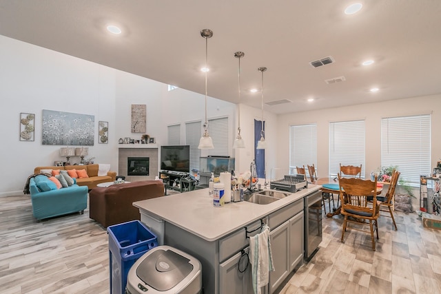 kitchen featuring sink, a kitchen island with sink, a tile fireplace, pendant lighting, and light hardwood / wood-style floors