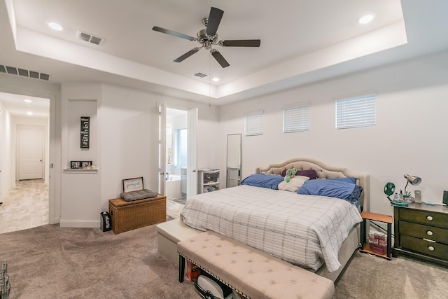 carpeted bedroom featuring ceiling fan, ensuite bathroom, and a raised ceiling