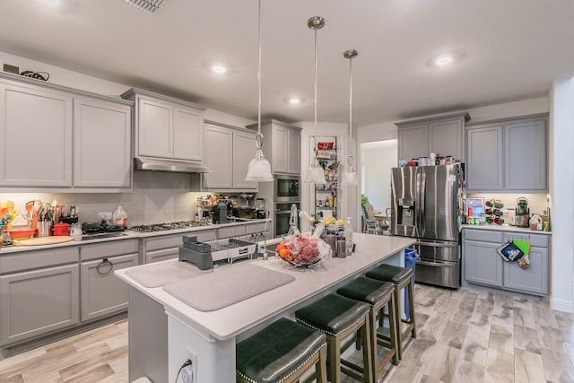 kitchen with appliances with stainless steel finishes, a kitchen breakfast bar, tasteful backsplash, a center island with sink, and decorative light fixtures