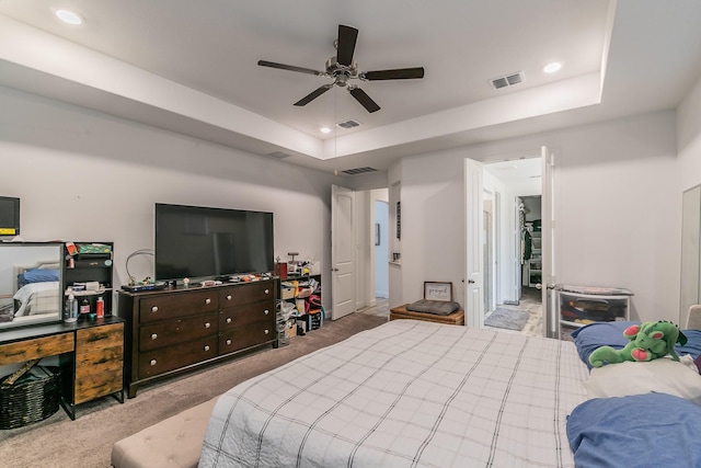 bedroom with light colored carpet, a raised ceiling, and ceiling fan