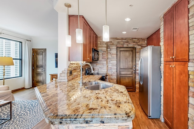 kitchen featuring sink, light hardwood / wood-style flooring, stainless steel refrigerator, decorative light fixtures, and kitchen peninsula