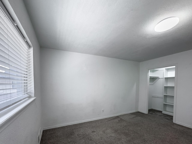 unfurnished bedroom with a textured ceiling, dark carpet, and a closet