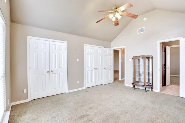 unfurnished bedroom featuring multiple closets, ceiling fan, light carpet, and high vaulted ceiling