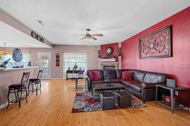 living room with ceiling fan with notable chandelier, a textured ceiling, and light hardwood / wood-style flooring