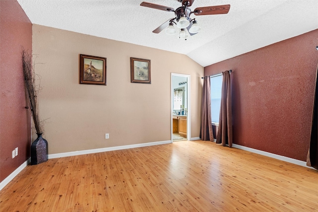 spare room with ceiling fan, lofted ceiling, a textured ceiling, and light wood-type flooring