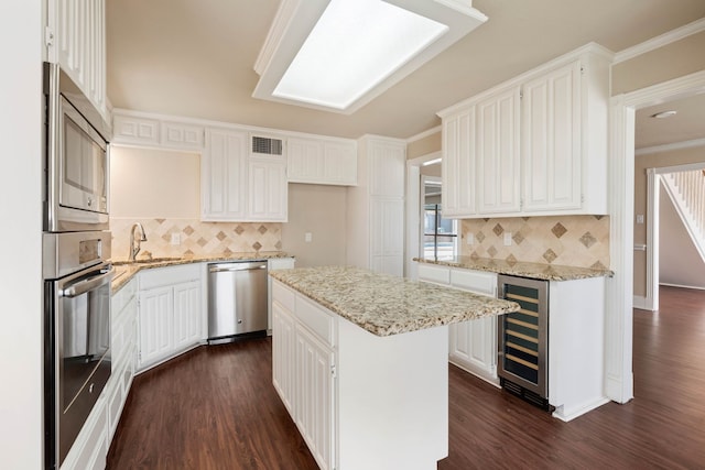 kitchen featuring appliances with stainless steel finishes, white cabinetry, light stone countertops, a kitchen island, and beverage cooler