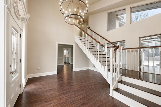 foyer entrance with an inviting chandelier, a towering ceiling, dark wood-type flooring, and a healthy amount of sunlight