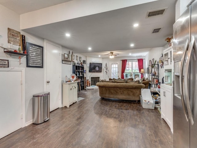 living room featuring ceiling fan, a large fireplace, and dark hardwood / wood-style flooring