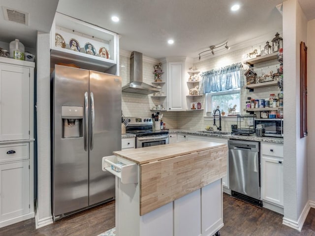 kitchen with butcher block countertops, appliances with stainless steel finishes, white cabinetry, a center island, and wall chimney exhaust hood