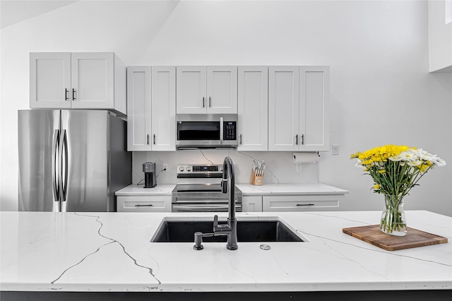 kitchen with appliances with stainless steel finishes, sink, lofted ceiling, and light stone counters