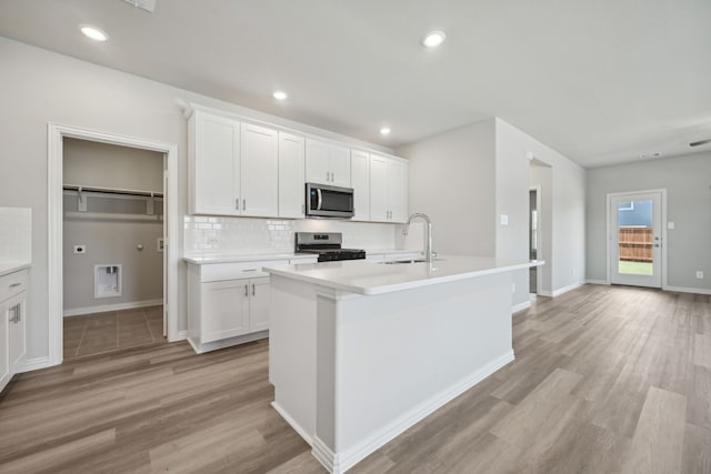 kitchen featuring light hardwood / wood-style flooring, appliances with stainless steel finishes, white cabinets, a kitchen island with sink, and backsplash