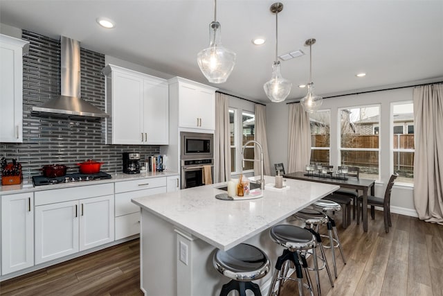 kitchen with white cabinetry, appliances with stainless steel finishes, an island with sink, and wall chimney range hood