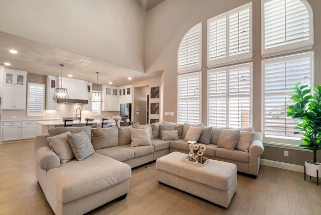 living room featuring light wood-type flooring, a towering ceiling, baseboards, and recessed lighting