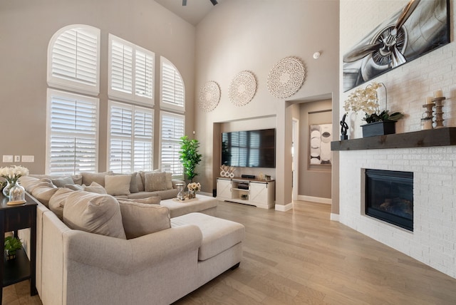 living area with light wood finished floors, baseboards, a fireplace, and a high ceiling