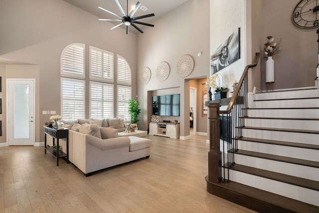 living room featuring light wood-style floors, baseboards, stairs, and a high ceiling