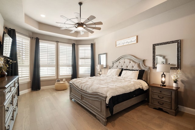 bedroom with baseboards, a tray ceiling, multiple windows, and light wood-style floors