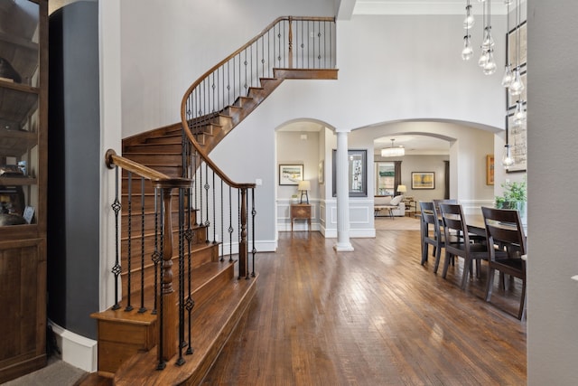 entryway with dark hardwood / wood-style flooring, crown molding, a high ceiling, and ornate columns