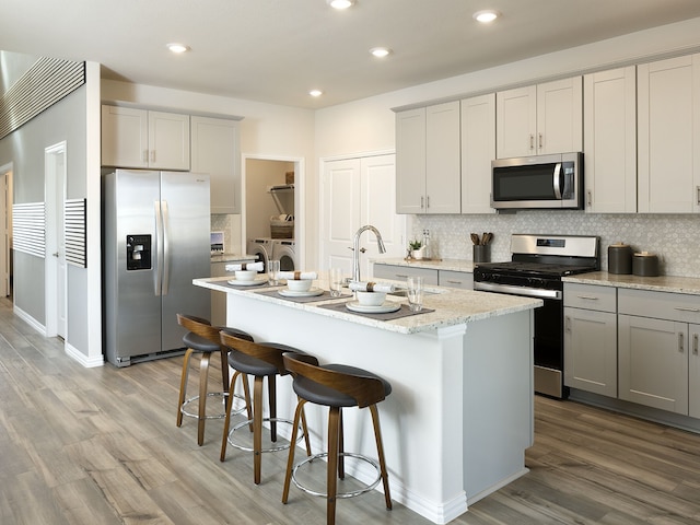 kitchen with stainless steel appliances, sink, a center island with sink, and decorative backsplash