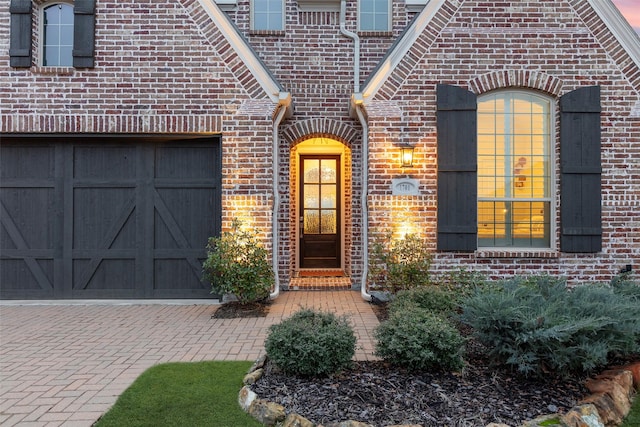 view of exterior entry with brick siding, decorative driveway, and an attached garage