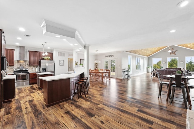 kitchen featuring a spacious island, tasteful backsplash, hanging light fixtures, appliances with stainless steel finishes, and wall chimney range hood