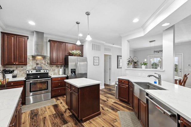 kitchen with stainless steel appliances, hanging light fixtures, sink, and wall chimney range hood