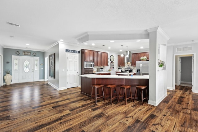 kitchen featuring dark wood-type flooring, a breakfast bar, hanging light fixtures, stainless steel appliances, and wall chimney exhaust hood