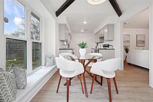 dining room featuring beam ceiling, plenty of natural light, and light hardwood / wood-style floors