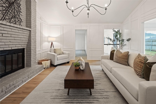 living room with wood-type flooring, lofted ceiling, an inviting chandelier, and a brick fireplace