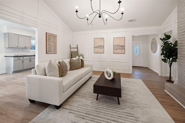 living room with light hardwood / wood-style flooring, a notable chandelier, and vaulted ceiling