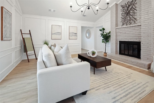 living room with lofted ceiling, crown molding, a fireplace, a chandelier, and light wood-type flooring