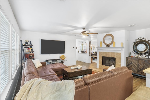 living room with ceiling fan, a tile fireplace, and light hardwood / wood-style flooring