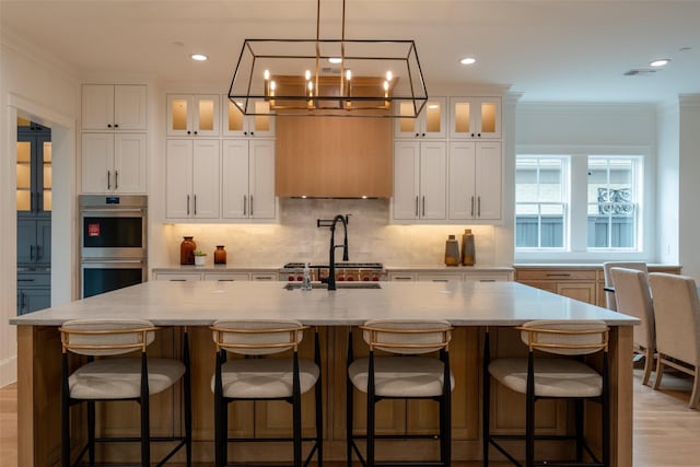 kitchen with a kitchen island with sink, double oven, a kitchen breakfast bar, and white cabinets