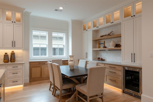 dining room featuring crown molding, beverage cooler, and light hardwood / wood-style flooring