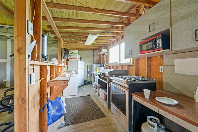 kitchen with high end range, wooden walls, stainless steel range with gas stovetop, white refrigerator, and separate washer and dryer