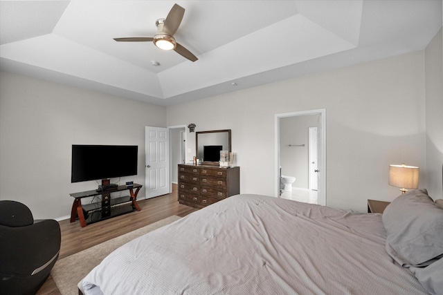 bedroom with ceiling fan, a raised ceiling, light hardwood / wood-style floors, and ensuite bath