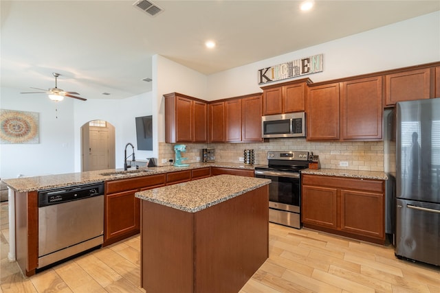 kitchen with sink, light stone counters, kitchen peninsula, a kitchen island, and stainless steel appliances