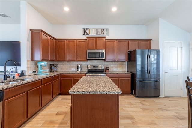 kitchen with sink, tasteful backsplash, appliances with stainless steel finishes, a kitchen island, and light stone countertops