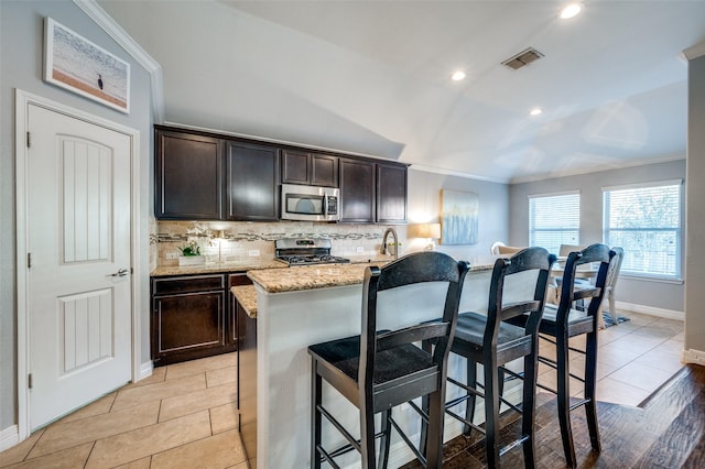 kitchen with a kitchen bar, light stone counters, crown molding, stainless steel appliances, and backsplash