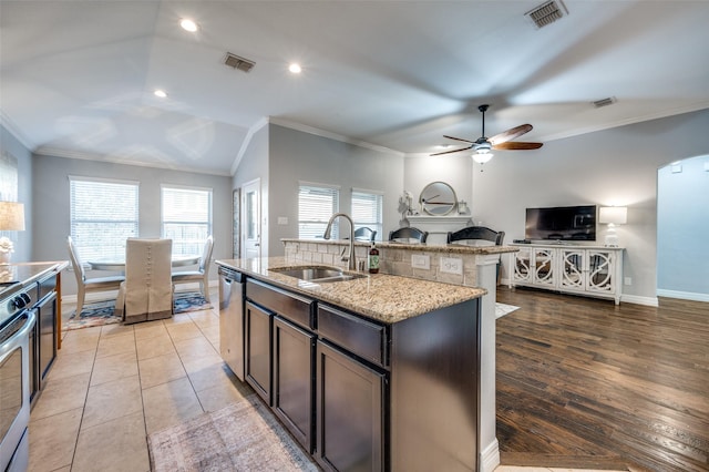 kitchen featuring sink, a center island with sink, ornamental molding, dishwasher, and light stone countertops