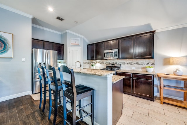 kitchen featuring light stone counters, stainless steel appliances, an island with sink, and dark brown cabinetry