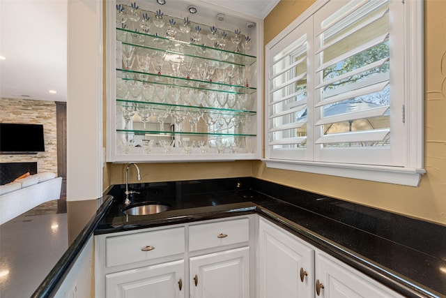 bar with sink, a fireplace, and white cabinets