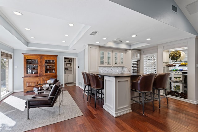 kitchen with dark hardwood / wood-style flooring, decorative backsplash, a raised ceiling, and a kitchen bar