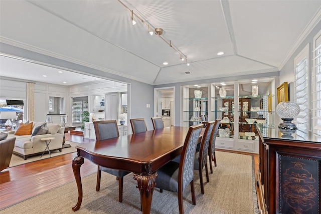 dining area with crown molding, lofted ceiling, rail lighting, and light hardwood / wood-style flooring