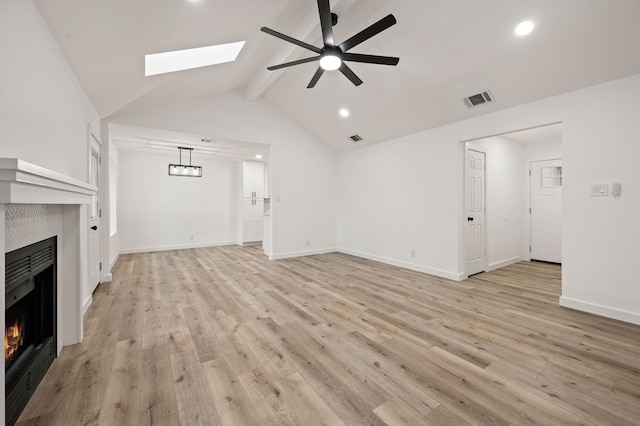 unfurnished living room with ceiling fan, vaulted ceiling with skylight, and light wood-type flooring