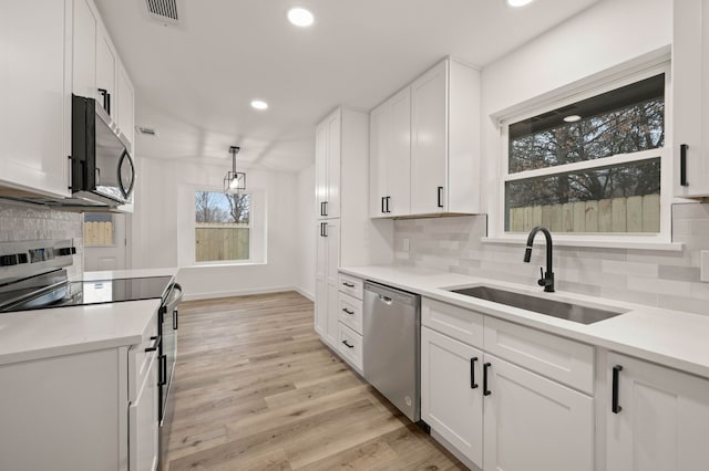 kitchen featuring sink, appliances with stainless steel finishes, white cabinetry, light hardwood / wood-style floors, and decorative light fixtures