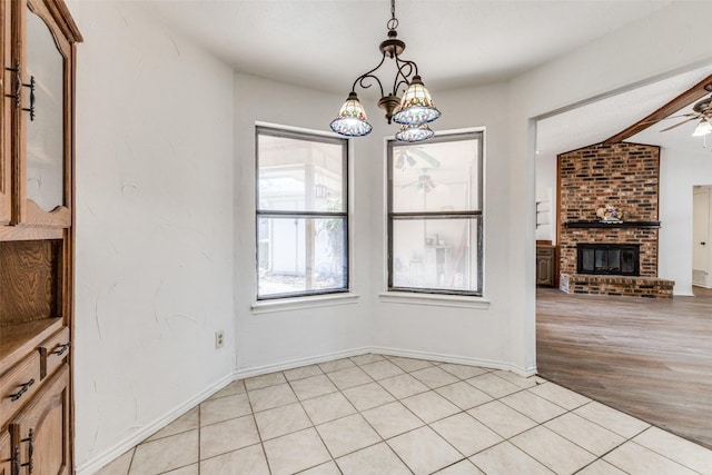 unfurnished dining area with lofted ceiling with beams, ceiling fan with notable chandelier, a fireplace, and light tile patterned floors