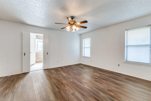 empty room with ceiling fan, a wealth of natural light, a textured ceiling, and dark hardwood / wood-style flooring